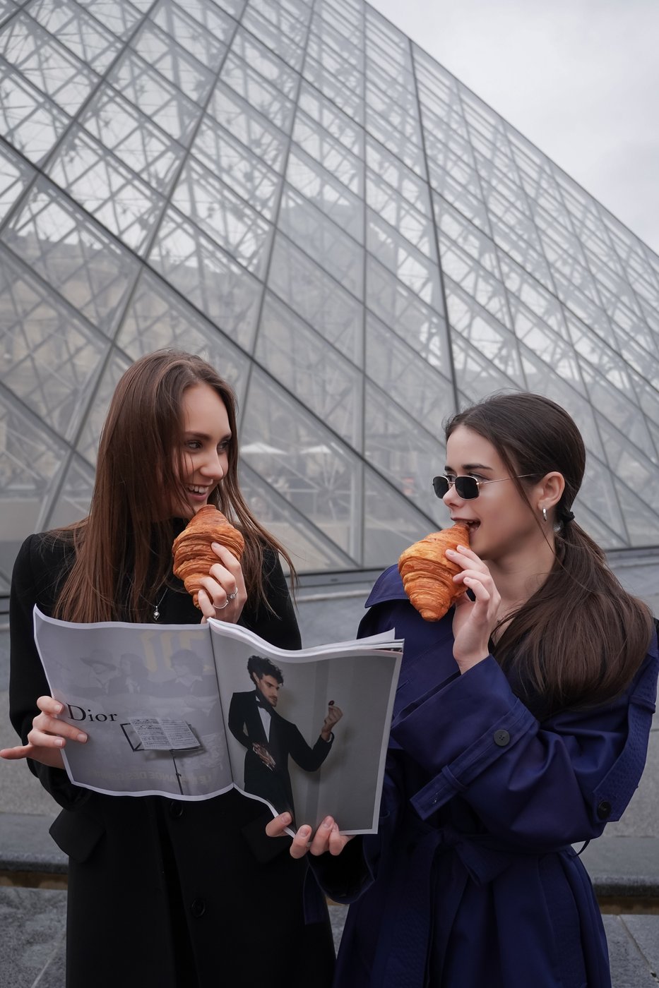 Two friends sharing croissants in front of the Louvre pyramid, Paris